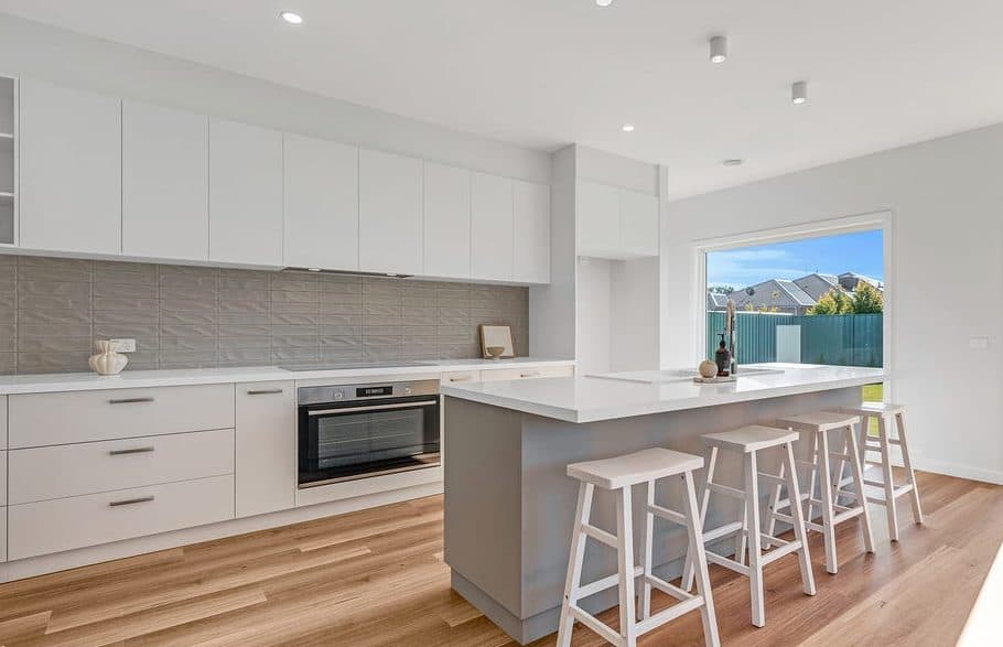 Kitchen styled for sale by Wisteria & Oak, with white cabinetry, a stone island bench and four white stools