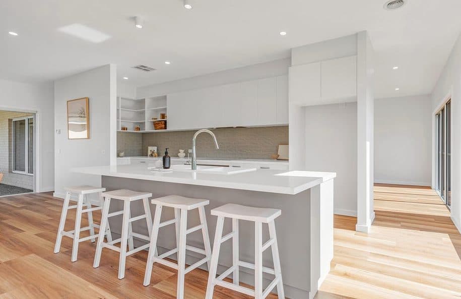 Open plan kitchen with a long island bench and four bar stools, styled for sale by Wisteria & Oak