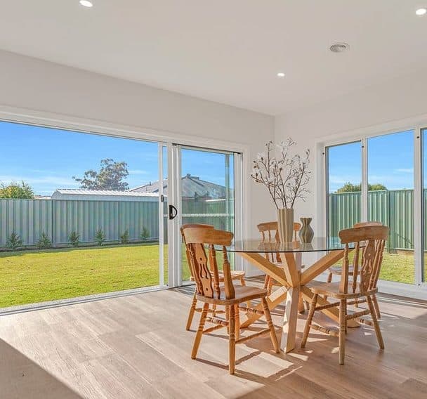 Dining table with timber chairs beside sliding doors opening to the backyard, styled for sale by Wisteria & Oak