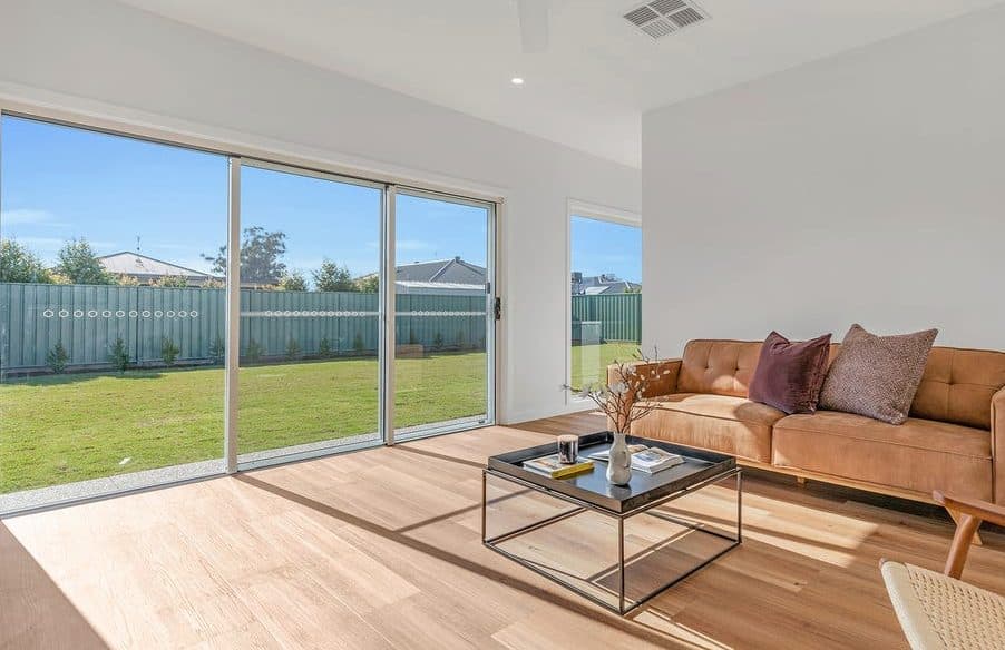 Living room styled for sale by Wisteria & Oak, with a tan leather sofa, a low glass coffee table and wide sliding doors to the garden