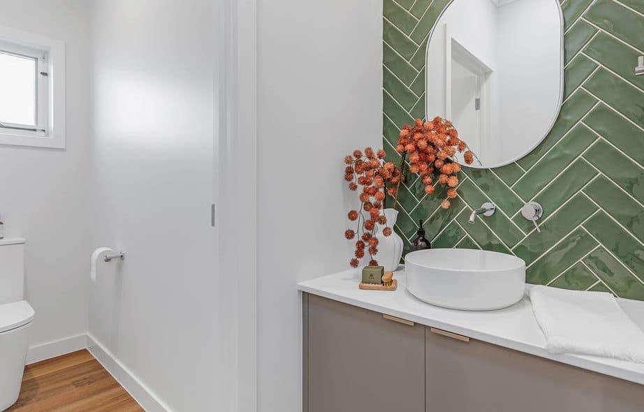 Powder room styled by Wisteria & Oak, with green herringbone tile, a round mirror, vessel basin and a dried floral arrangement