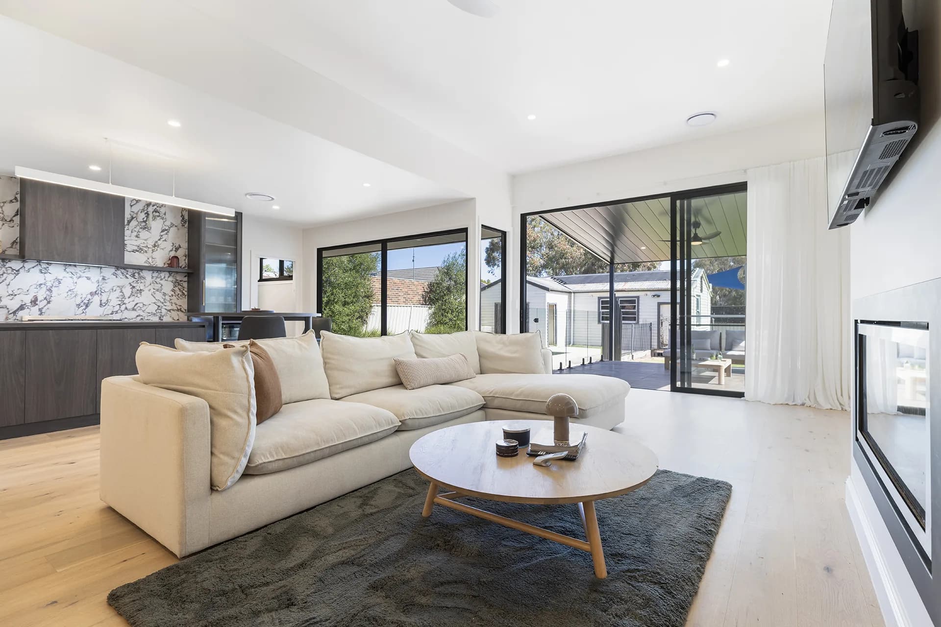 Living room with a pale modular sofa, round coffee table and doors to the covered deck at Hare Street, Echuca