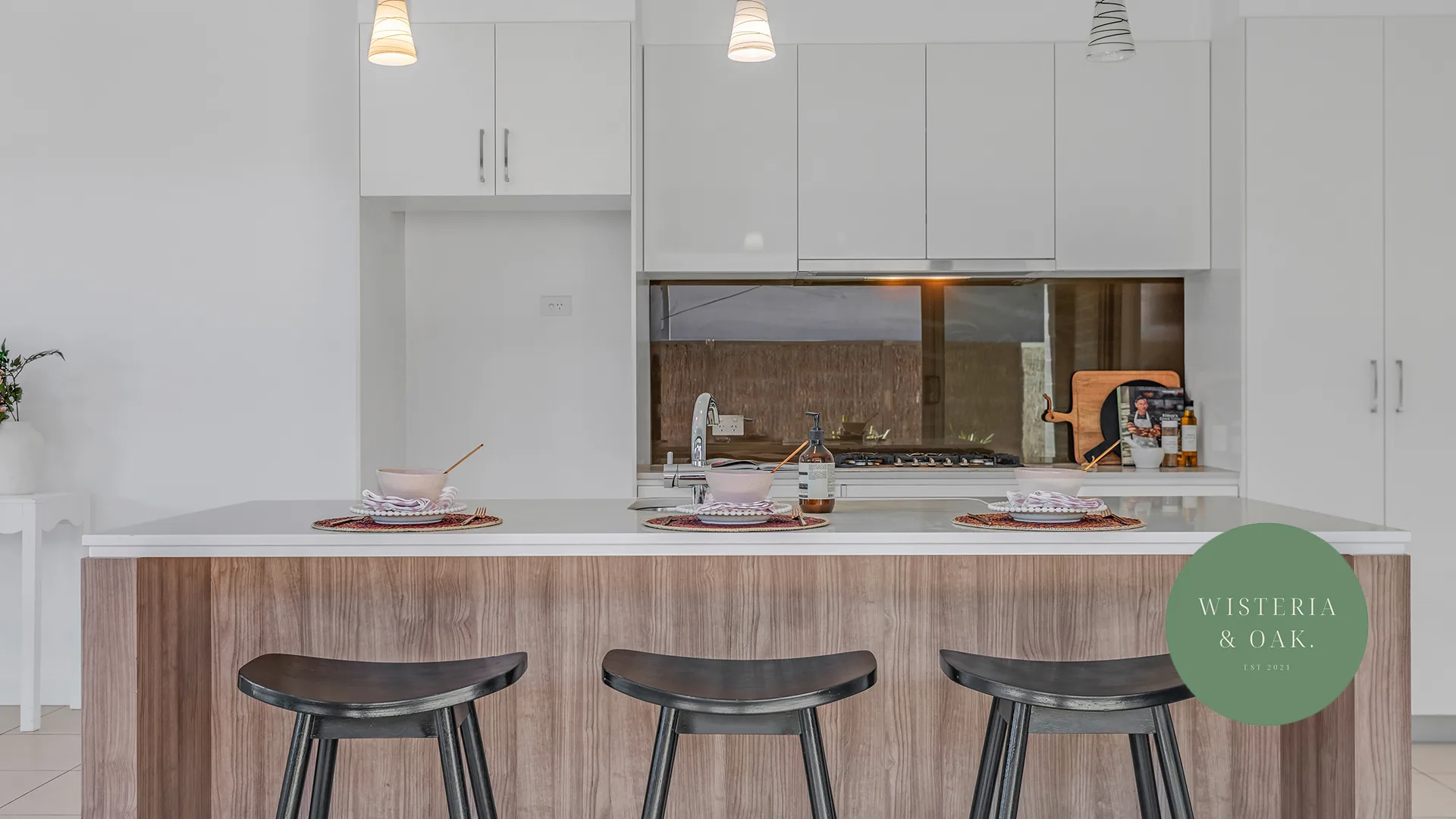 Kitchen with a timber island bench, black stools and a tiled splashback at Maiden Street, Moama